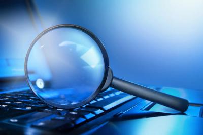 magnifying glass atop laptop keyboard in blue lighting